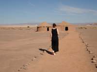 Traditional huts in the Atacama Desert with a lone traveler walking across the sandy landscape under clear skies. 