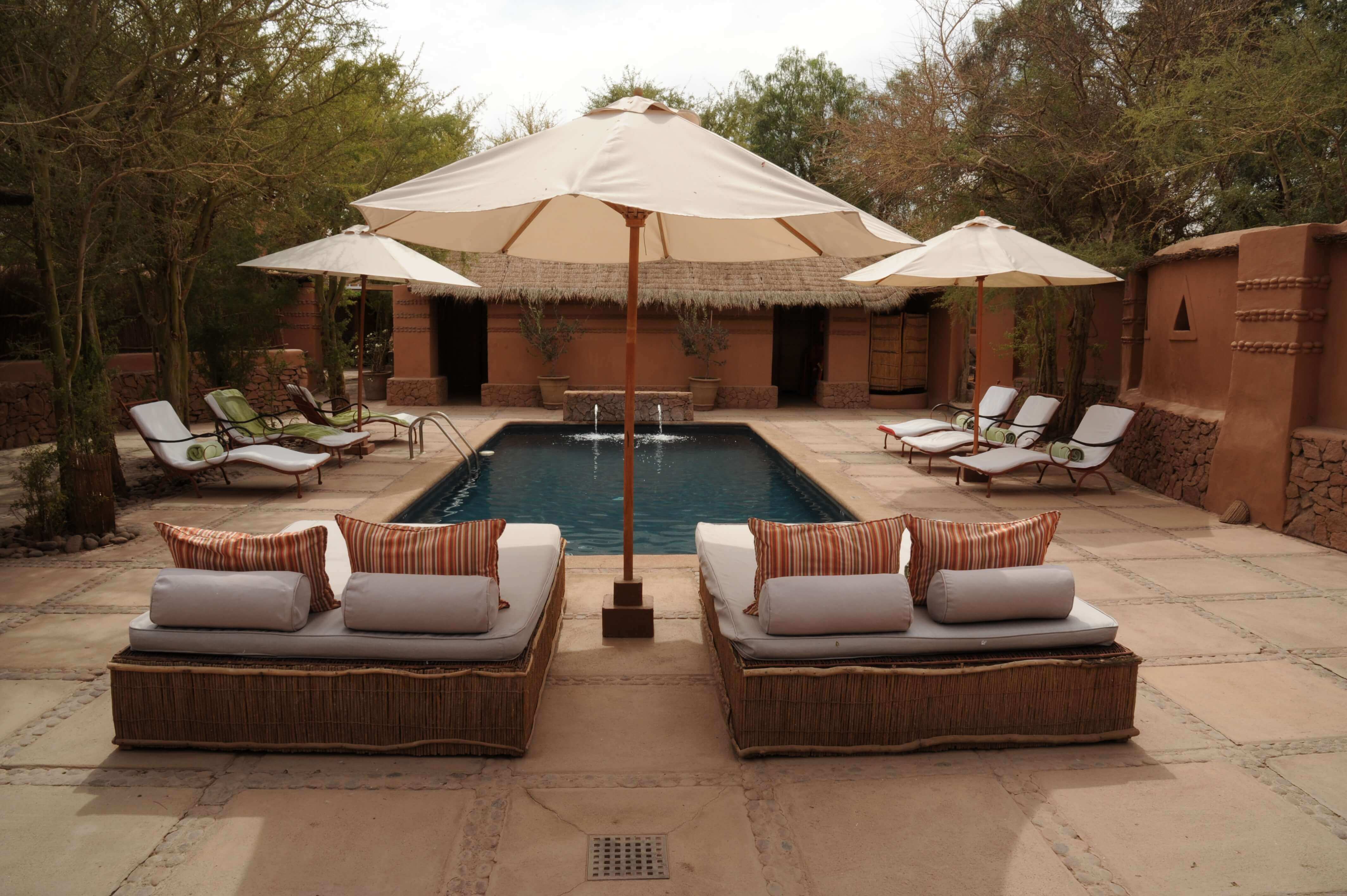 Relaxing poolside loungers and parasols in a stylish desert retreat, perfect for unwinding in Chile's Atacama region. 