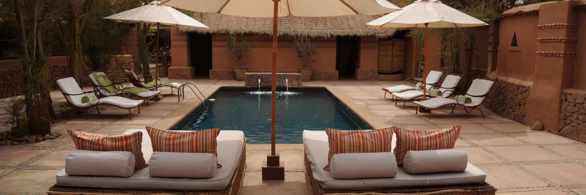 Relaxing poolside loungers and parasols in a stylish desert retreat, perfect for unwinding in Chile's Atacama region. 