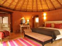 A spacious luxury hotel room in Chile's Atacama Desert features warm earth tones, a thatched ceiling, and elegant decor. 