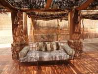 A cozy lounge with rustic cushions sits beneath a woven shade roof in the warm desert ambiance of Chile's Atacama region. 