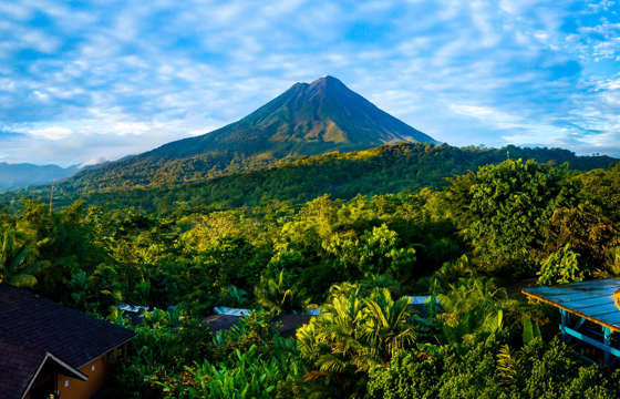Arenal Volcano rises above the tropical forest of Costa Rica, framed by colorful lodges. 
