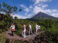 Hikers explore the rugged trails beneath Arenal Volcano's iconic peak in lush Costa Rican scenery. 