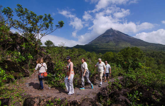 Hikers explore the rugged trails beneath Arenal Volcano's iconic peak in lush Costa Rican scenery. 