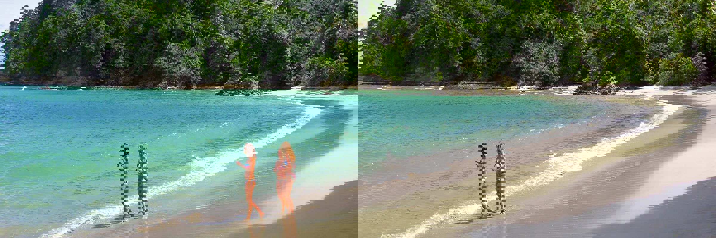 Tourists stroll along the pristine shores of Manuel Antonio, embraced by rainforest and turquoise sea. 
