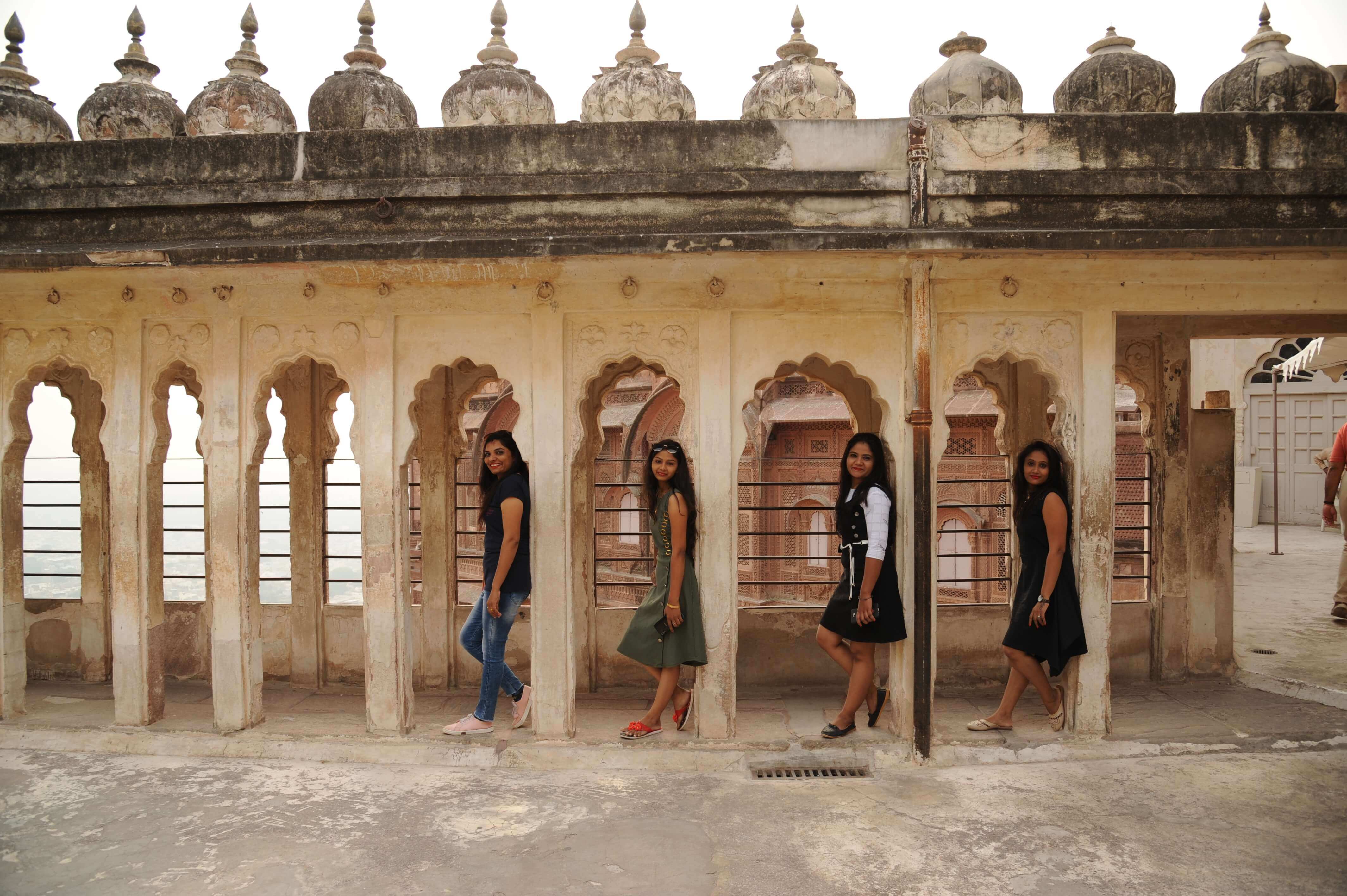 India- Young women exploring heritage architecture with Mughal-style arches in a historic palace. 