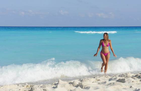 Woman walking out of turquoise waters onto white sands at Playa del Carmen beach, Riviera Maya, Mexico. 