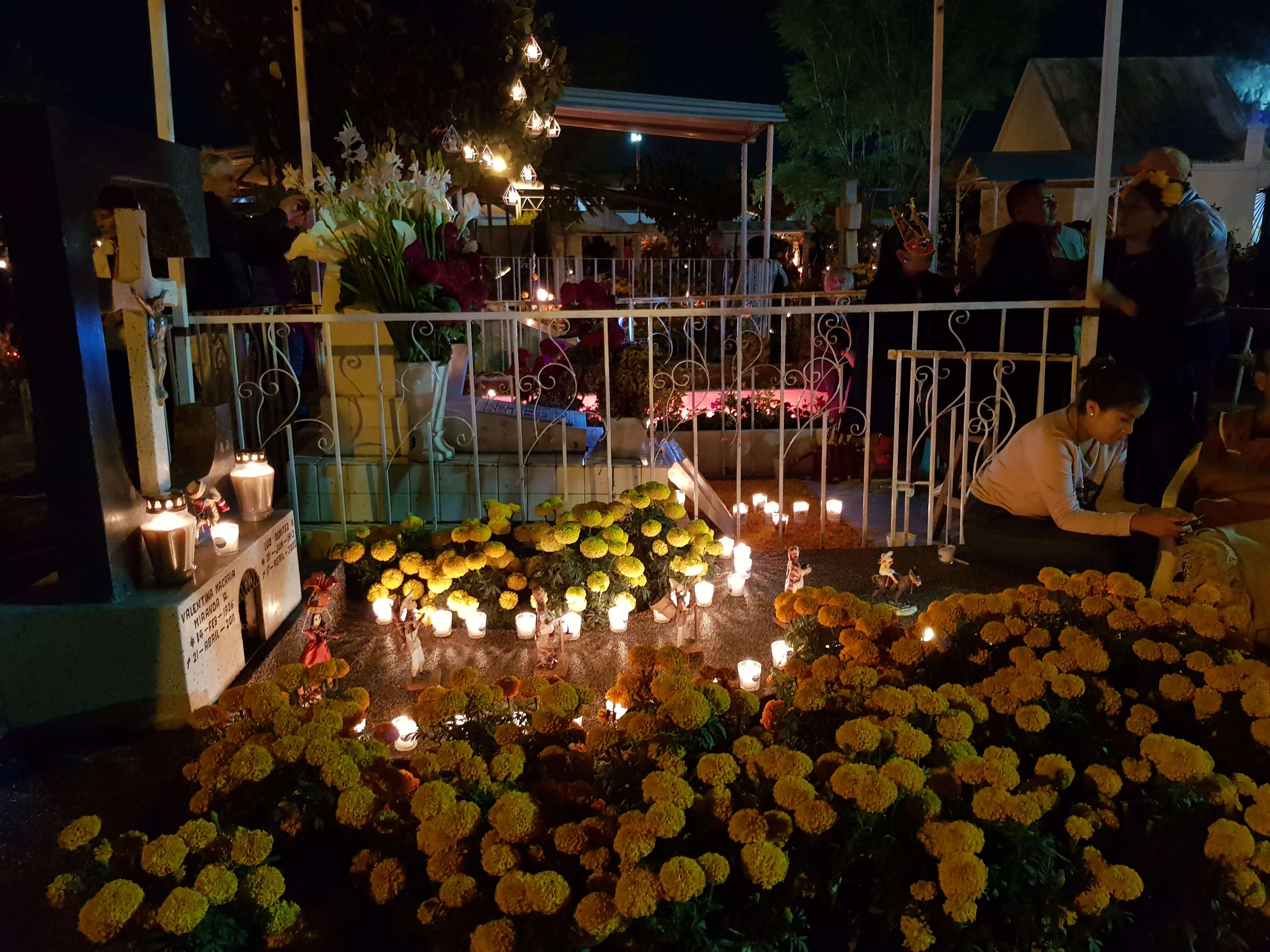 Day of the Dead cemetery altar in Mexico, decorated with marigold flowers, candles, and photos during a nighttime vigil. 