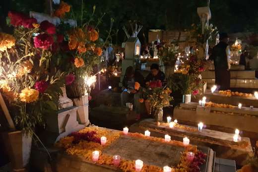 Decorated graves in a Mexican cemetery during Day of the Dead, with candles, marigolds, and families gathered to honour love ones. 