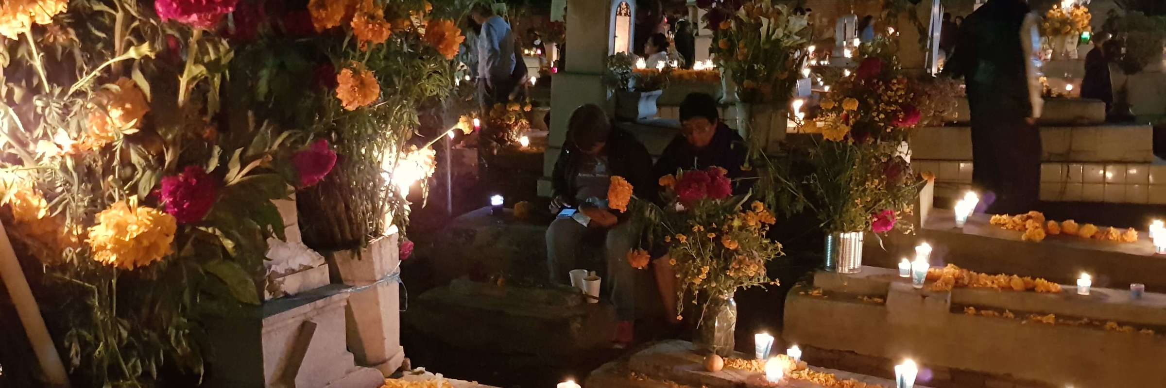 Decorated graves in a Mexican cemetery during Day of the Dead, with candles, marigolds, and families gathered to honour love ones. 