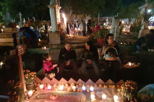 A Mexican family gathered at a candlelit grave during Day of the Dead, honouring ancestors with flowers an offerings. 
