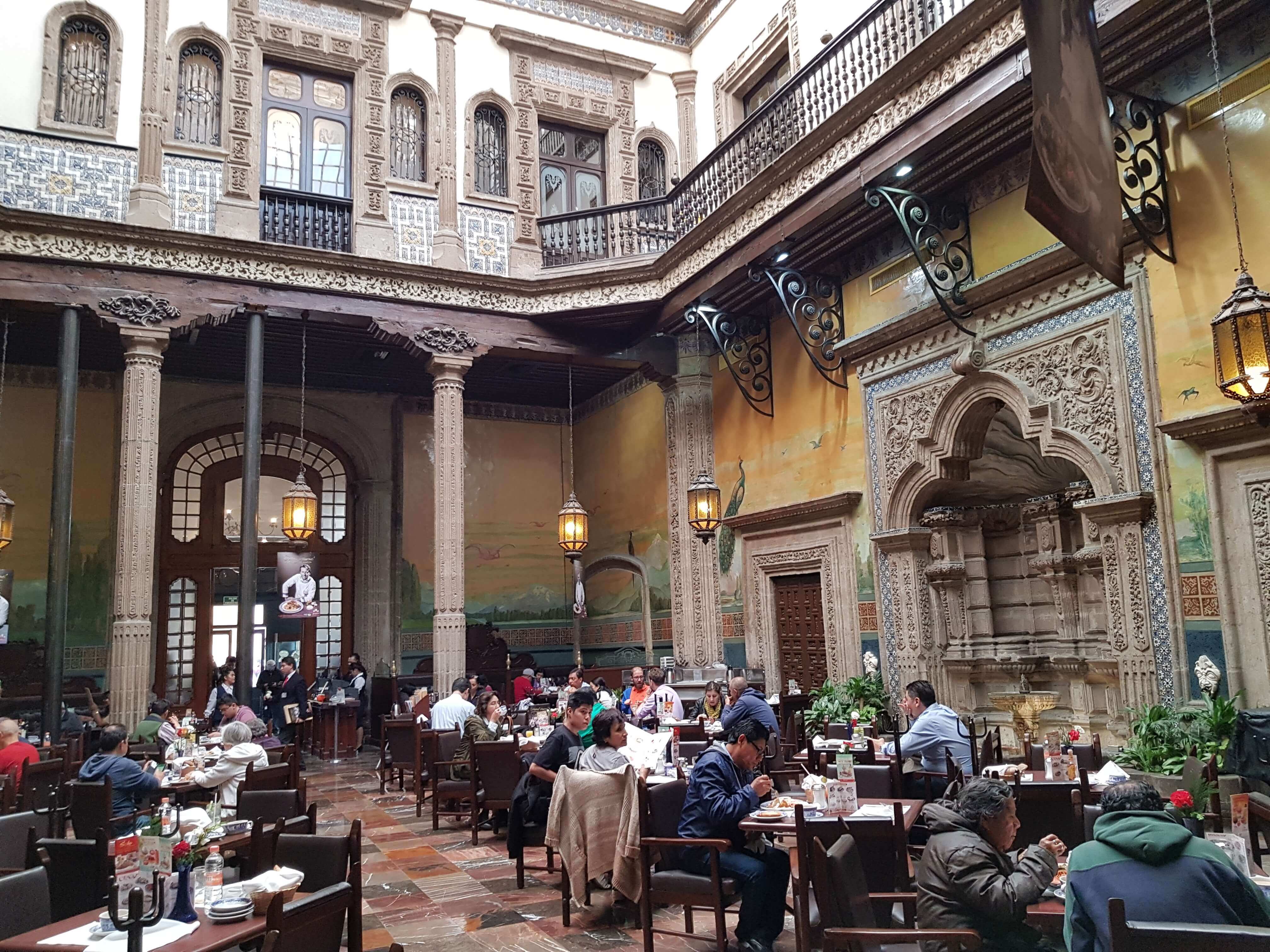 Guests dining in a historic Mexico City restaurant with colonial architecture, detailed stonework, and vibrant murals. 