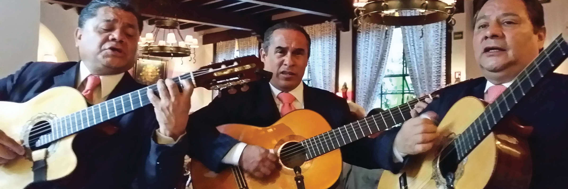 Three traditional Mexican guitarists perform indoors, capturing the spirit and musical heritage of Mexico. 
