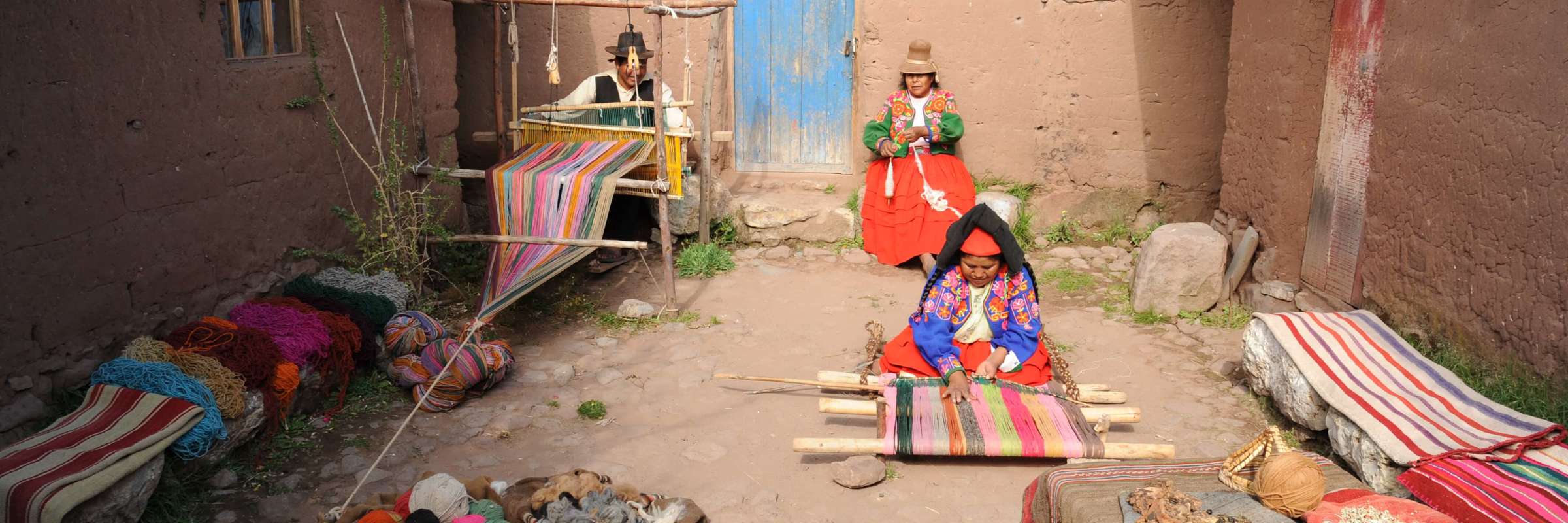 A family gathers in a quiet courtyard, surrounded by woven blankets and rural charm near Lake Titicaca. 
