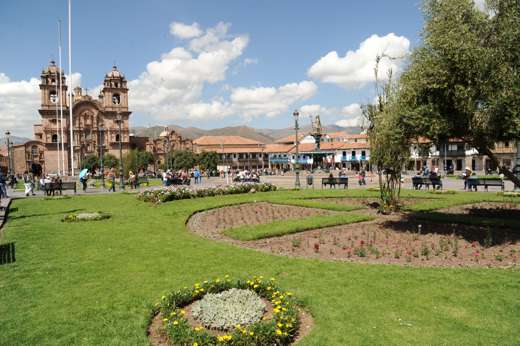 Cusco's Plaza de Armas with colonial architecture and vibrant gardens under a blue sky. 