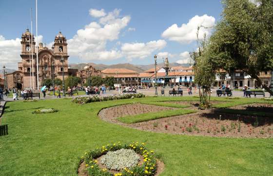 Cusco's Plaza de Armas with colonial architecture and vibrant gardens under a blue sky. 