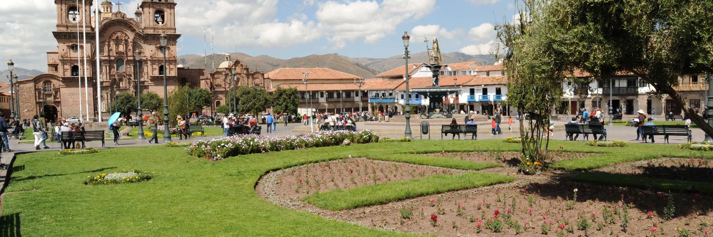 Cusco's Plaza de Armas with colonial architecture and vibrant gardens under a blue sky. 