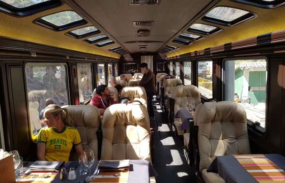 Passengers relax in comfort aboard a scenic train bound for Cusco, framed by panoramic Andean views. 