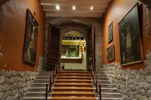 Interior of a colonial-era convent in Cusco, Peru, with stone walls, artwork, and wooden doors. 