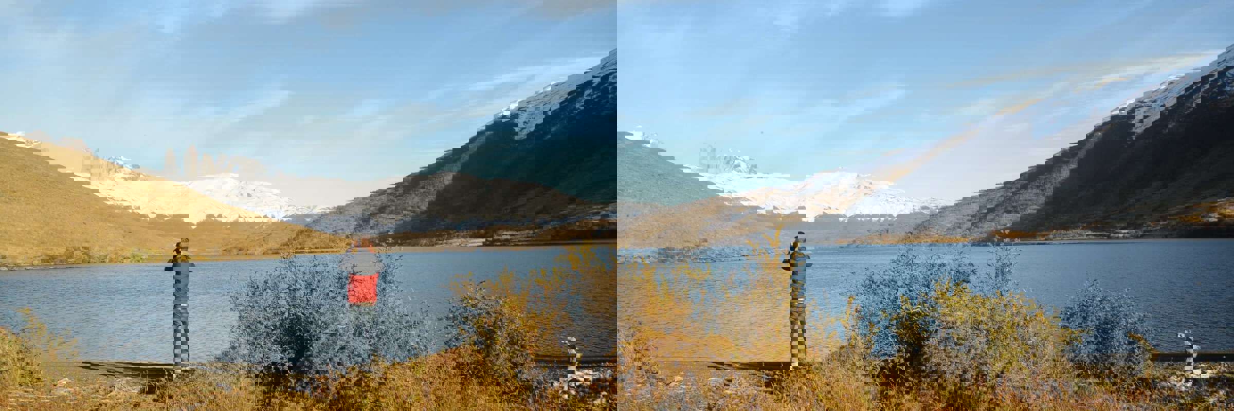 A traveler photograph the serene lake and jagged snow-capped peaks of Torres del Paine in Chilean Patagonia under a wide blue sky. 