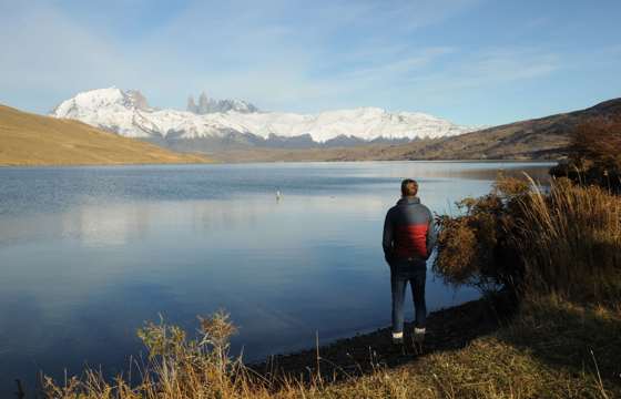 Traveler admires the reflection of the Paine Massif in a still Patagonia lake under clear skies in Torres del Paine, Chile. 