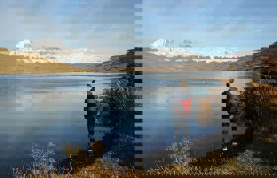 Traveler admires the reflection of the Paine Massif in a still Patagonia lake under clear skies in Torres del Paine, Chile. 