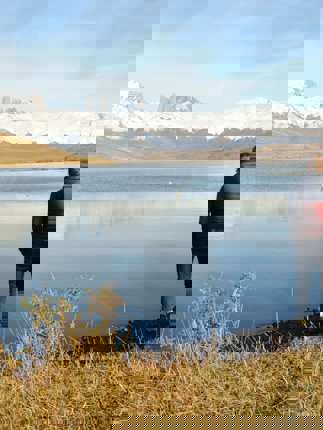 A lone visitor stands beside a still lake reflecting snow-capped peaks in Chile's Torres del Paine National Park. 