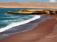 Red Beach in Paracas Reserve, where vibrant red sands meet turquoise waters along Peru's dramatic coast. 