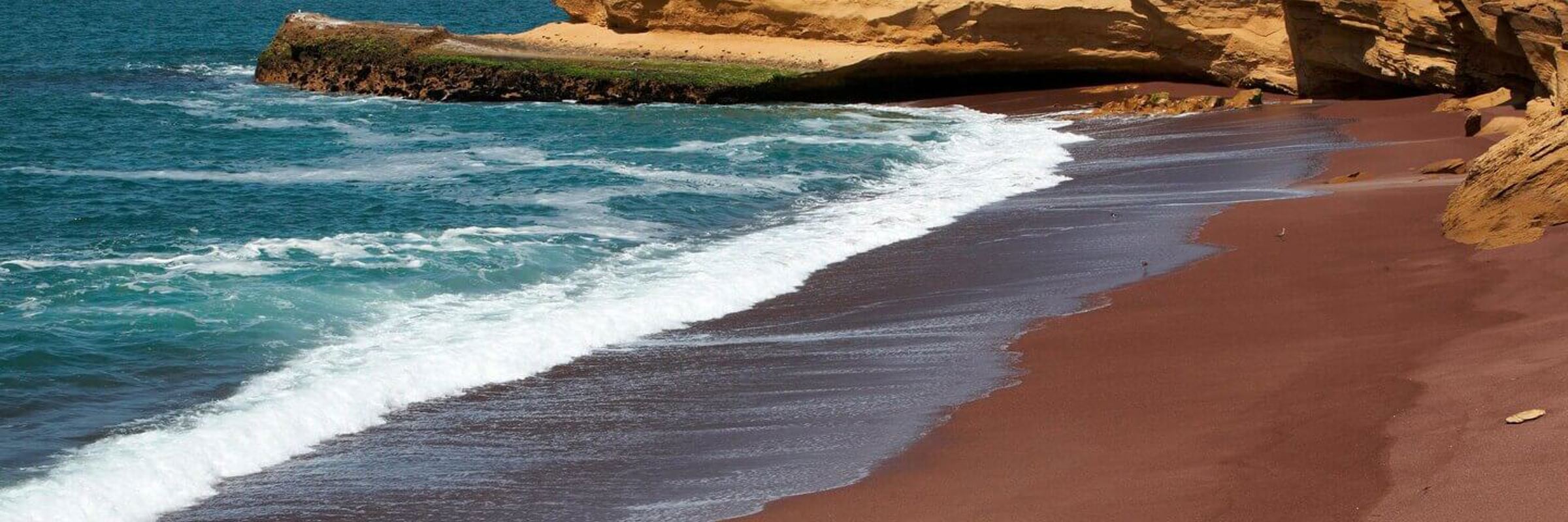 Red Beach in Paracas Reserve, where vibrant red sands meet turquoise waters along Peru's dramatic coast. 