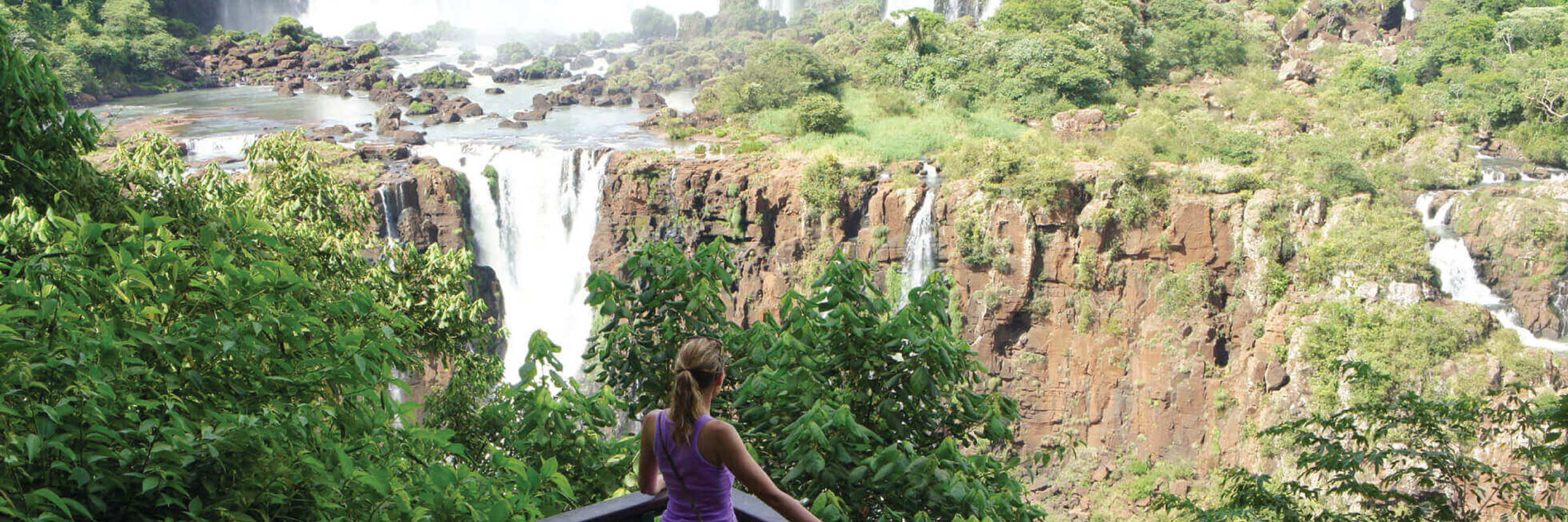 A visitor gazes across the panoramic Iguassu Falls, surrounded by lush Atlantic rainforest. 