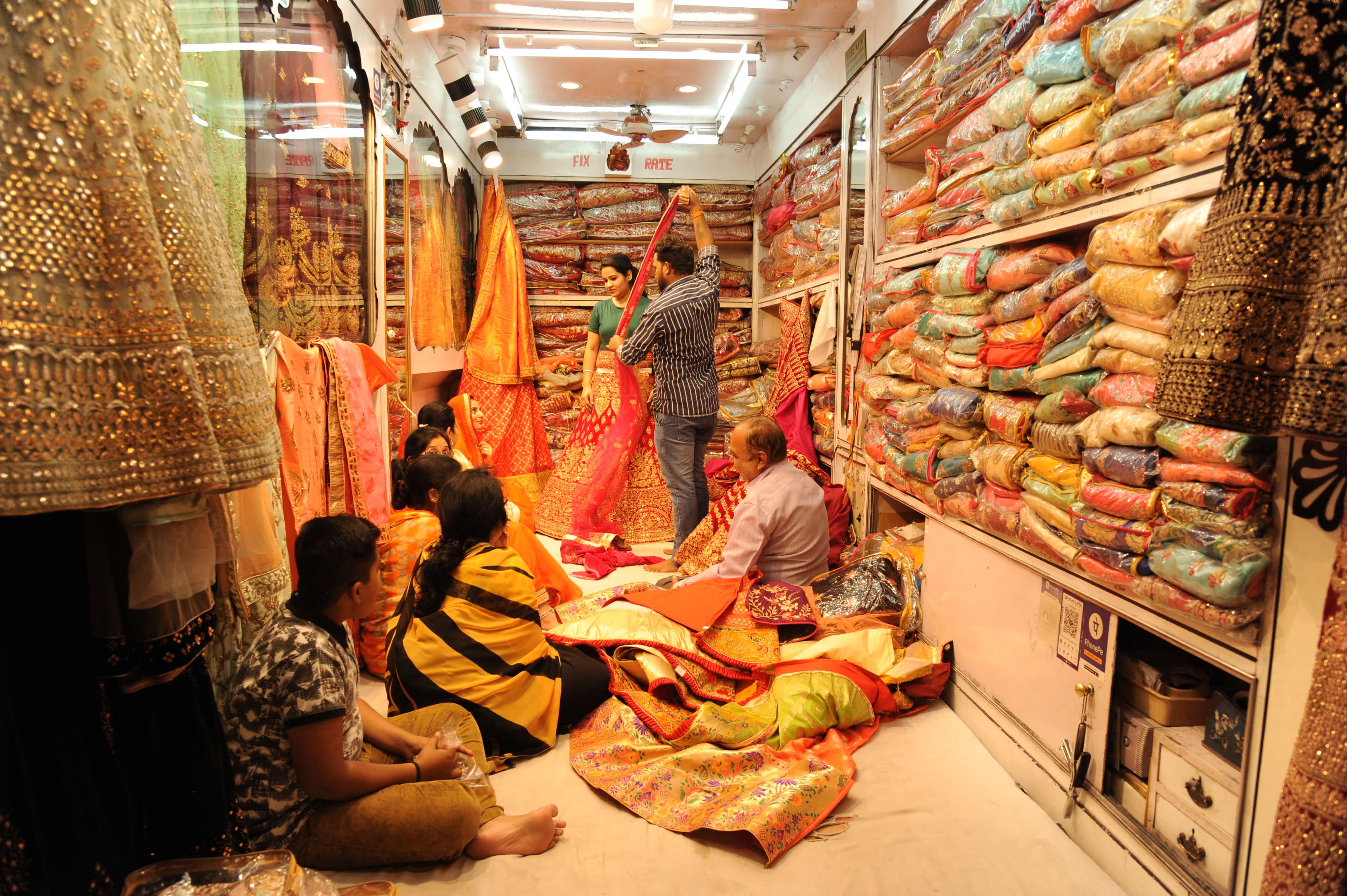 India- Women shopping for colourful saris in a traditional fabric store full of vibrant textiles. 