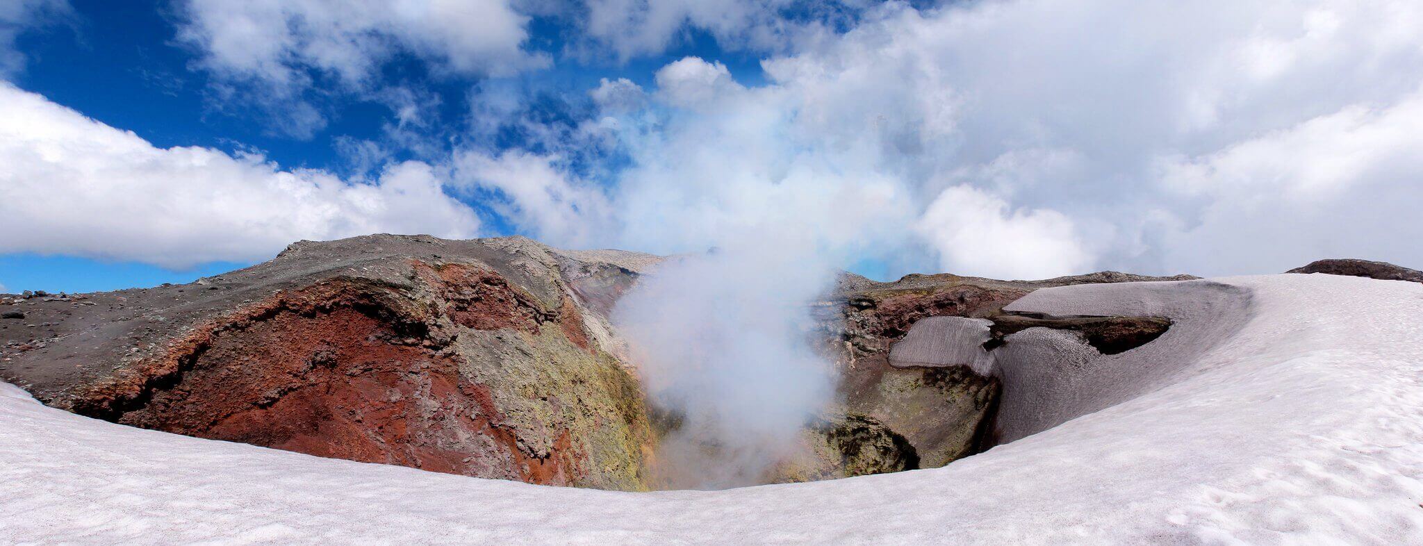 View of the steaming crater of Villarrica Volcano near Pucon, Chile, surrounded by snow and dramatic skies. 