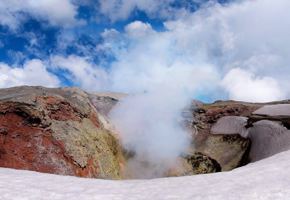 View of the steaming crater of Villarrica Volcano near Pucon, Chile, surrounded by snow and dramatic skies. 