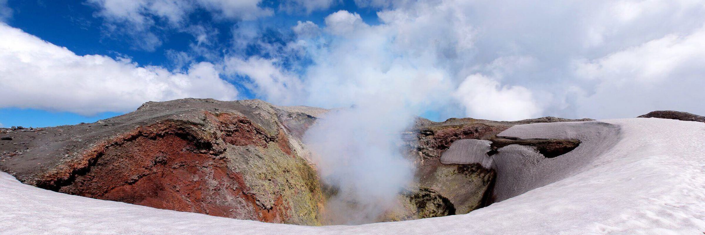 View of the steaming crater of Villarrica Volcano near Pucon, Chile, surrounded by snow and dramatic skies. 