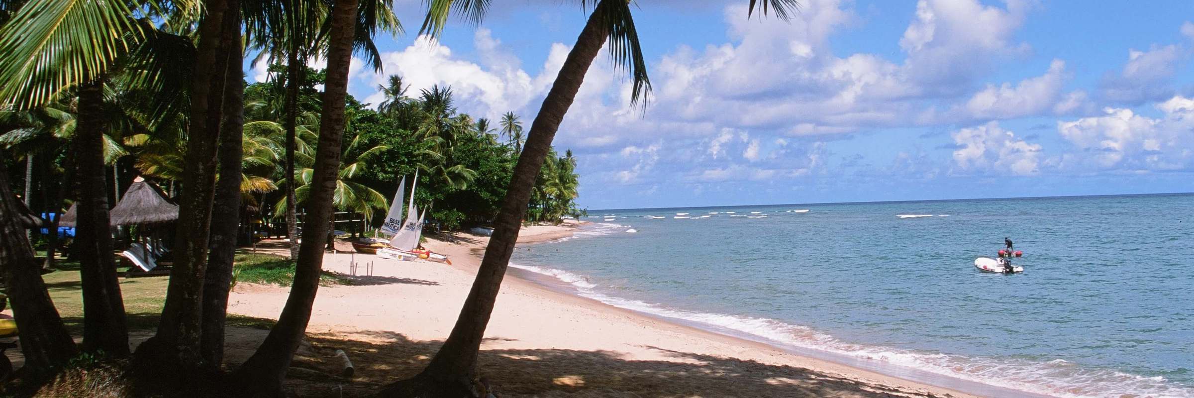 Palm-fringed white sand beach and calm blue sea at Praia do Forte in Bahia, Brazil. 