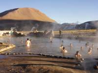 Travelers soak in El Tatio hot springs, surrounded by Andean peaks and rising steam near San Pedro de Atacama. 