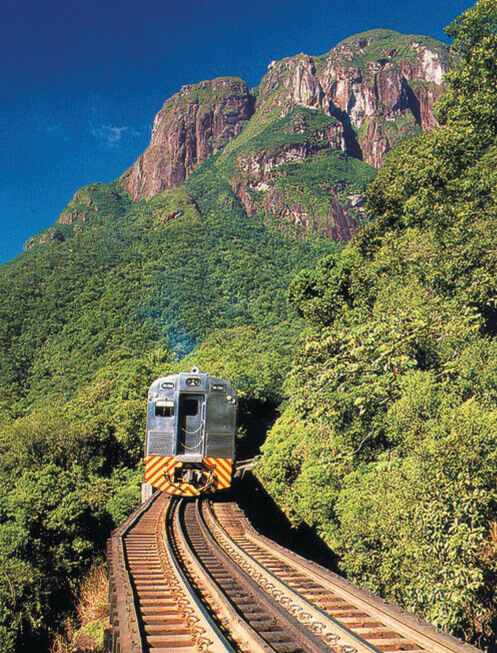 Serra Verde Express train travels through lush green hills and rocky mountains near Curitiba, Brazil. 