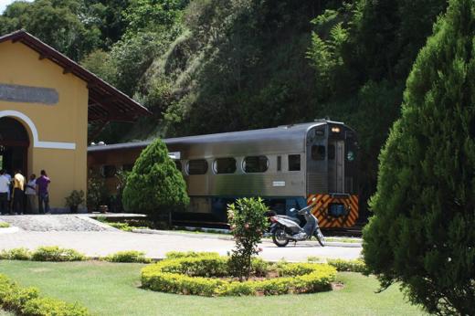 Serra Verde Express train arriving at a scenic station near Curitiba, surrounded by gardens and forested hills. 