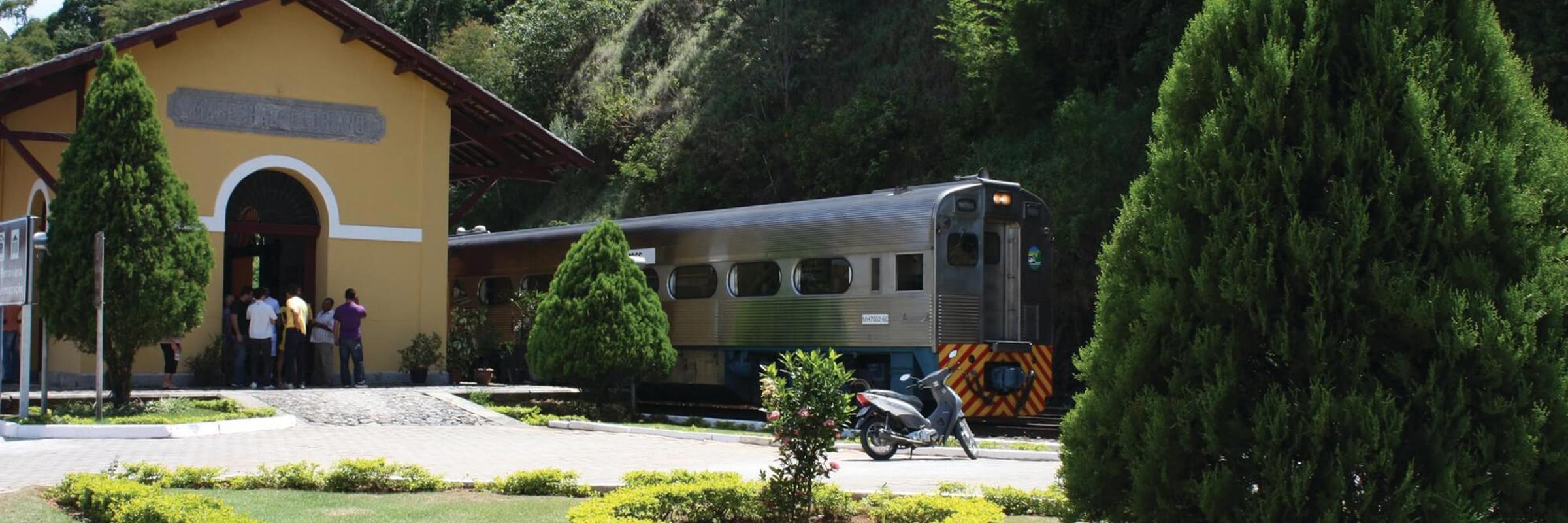 Serra Verde Express train arriving at a scenic station near Curitiba, surrounded by gardens and forested hills. 