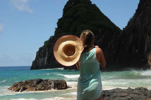 Woman with sunhat overlooks ocean and cliffs at Fernando de Noronha, a stunning island destination in Brazil. 