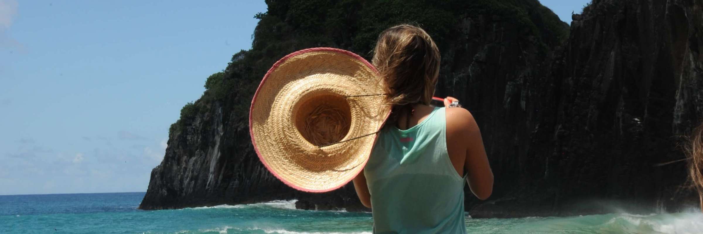 Woman with sunhat overlooks ocean and cliffs at Fernando de Noronha, a stunning island destination in Brazil. 