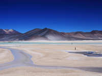 Vast salt flats with volcanoes in the distance under a deep blue sky in the Atacama Desert. 