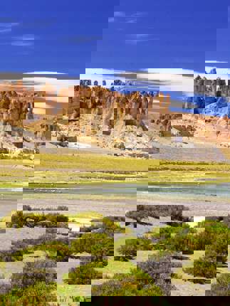 Dramatic rocks spires rise above green shrubs and a salt flat in Chile's high altitude Altiplano region. 