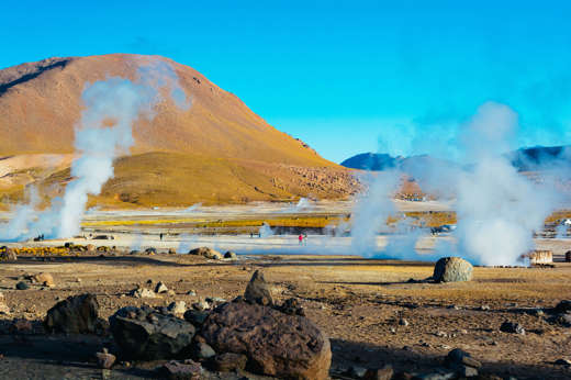 Steam rises from El Tatio geysers in Chile's Atacama Desert, surrounded by rocky terrain and golden morning light. 