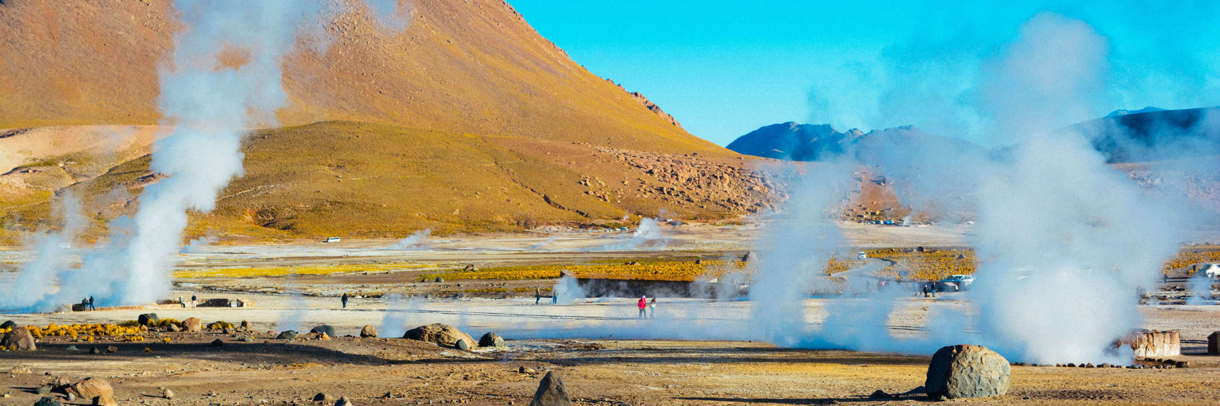 Steam rises from El Tatio geysers in Chile's Atacama Desert, surrounded by rocky terrain and golden morning light. 