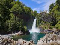 A waterfall cascades into a turquoise pool surrounded by lush forest in Chile's scenic Lake District. 