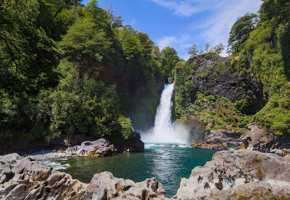 A waterfall cascades into a turquoise pool surrounded by lush forest in Chile's scenic Lake District. 
