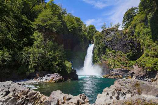 A waterfall cascades into a turquoise pool surrounded by lush forest in Chile's scenic Lake District. 