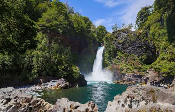 A waterfall cascades into a turquoise pool surrounded by lush forest in Chile's scenic Lake District. 