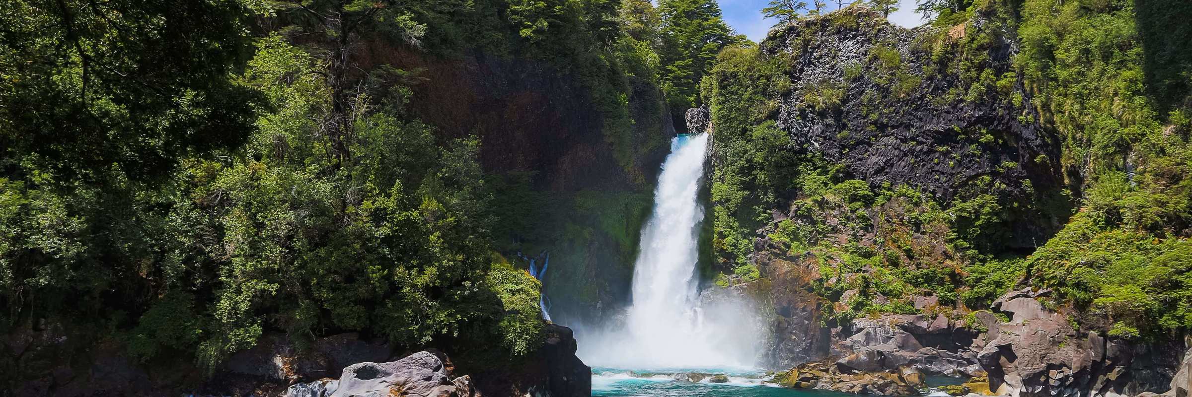 A waterfall cascades into a turquoise pool surrounded by lush forest in Chile's scenic Lake District. 